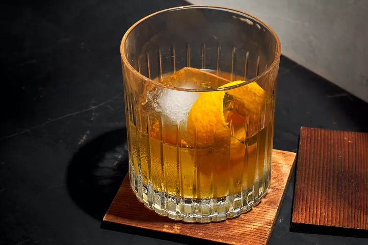 Mr.J cocktail in a glass with an orange color, ice and a orange peel strip