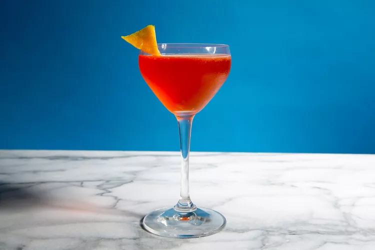 Paper Plane cocktail in a cup with an red and orange color twist and a cherry