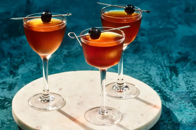 Manhattan cocktail in a cup with an orange and brown color twist and a cherry