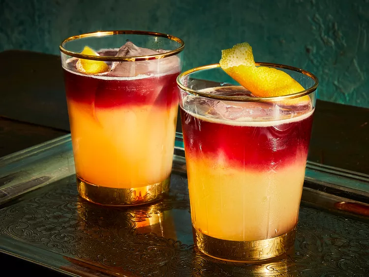 Two glasses containing the new-york-sour cocktail in red and yellow colors with ice and lemon
